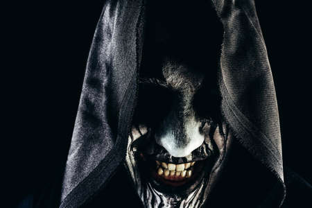 Horror photo of a male monster reaper smiling face in hood on dark background.の写真素材