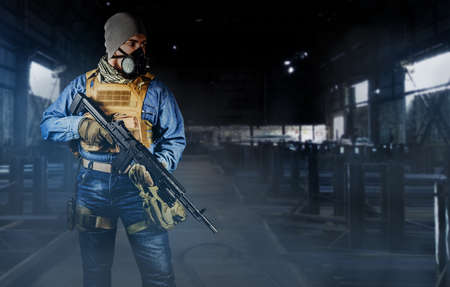 Photo of urban soldier in tactical military outfit and gas mask standing with rifle and gas mask on dark factory background.の写真素材