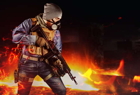 Photo of urban soldier in tactical military outfit and gas mask standing with rifle and gas mask on dark destroyed and burning city background.の写真素材