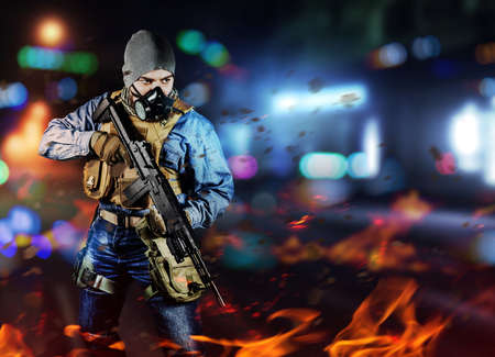Photo of urban soldier in tactical military outfit and gas mask standing with rifle and gas mask on night neon city and burning background.の写真素材