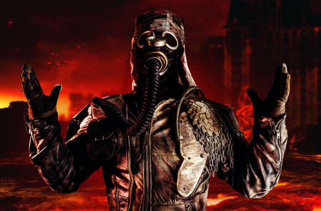 Photo of fantasy post apocalyptic warrior with armored outfit jacket, gas mask and scrap crown standing and praying on destroyed and burning city background.の写真素材