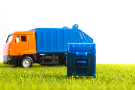 Photo of toy garbage truck with blue colored container on green lawn and white background.の写真素材