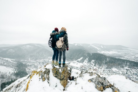 Rear view of happy friends hugging while walking in a snowy park or forest outdoor. Winter fun, vacation holidays. Love relationship people lifestyle conceptの写真素材
