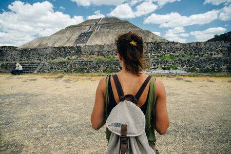 Teotihuacan, Mexico. A Mexican American tourist with a backpack and hat enjoys the view from the top of the Moon Pyramid. The Sun Pyramid and Avenue of the Dead can be seen in the distance.の写真素材