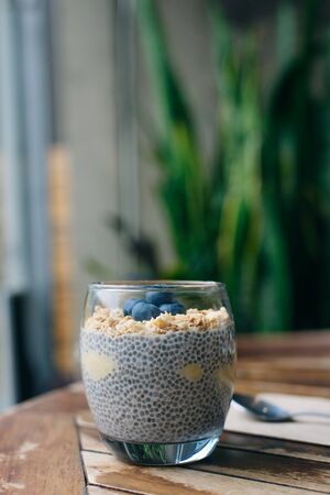 blueberry yogurt parfait with granola, oats and chia seeds in a glass on white wooden table