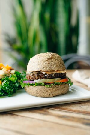 Vegan big burger with salad and piclkes in classic bun, served on white plate. Homemade healthy fast food.の写真素材