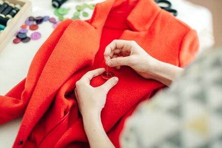 a seamstress sews a button on a red coat.の写真素材