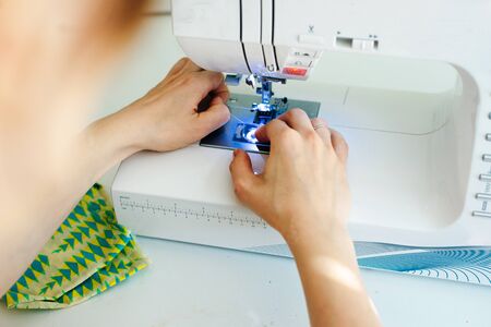 Female hands stitching white fabric on professional manufacturing machine at workplace. Seamstress hands holding textile for dress productionの写真素材