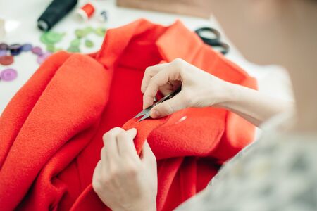 a seamstress sews a button on a red coat.