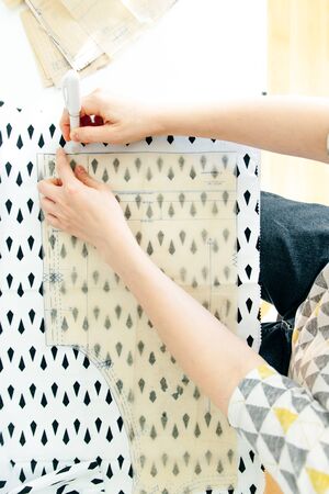 Top view of workplace of seamstress. Dressmaker cuts detail on sketch. Seamstress cuts pink fabric...