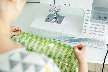 Female hands stitching white fabric on professional manufacturing machine at workplace. Seamstress...