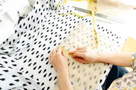 Top view of workplace of seamstress. Dressmaker cuts detail on sketch. Seamstress cuts pink fabric...