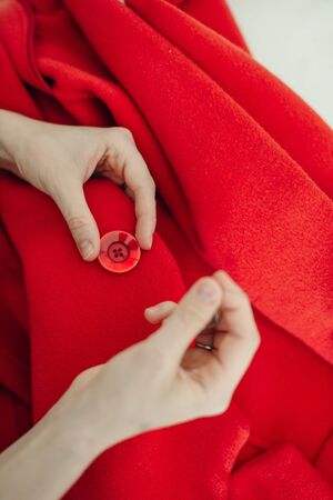 a seamstress sews a button on a red coat.