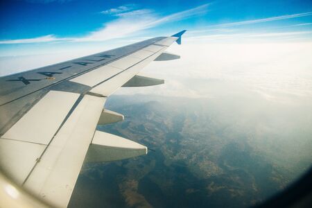 Plane window view of clouds and islands surrounded by sea and airplane wing. Traveling concept.