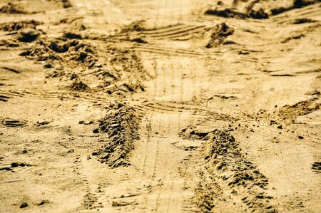 The tread marks of the tires of a large truck on yellow sand.