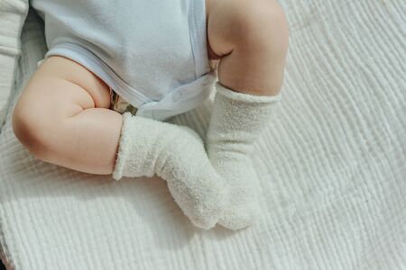 Baby legs. Crawling baby in white socks and bodysuit. View from above. Copy space.