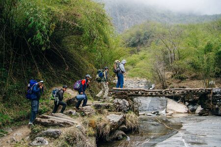 nepal - september, 2019 Group of travelers walks on bridge in Himalayas. Hikers with backpack goes...
