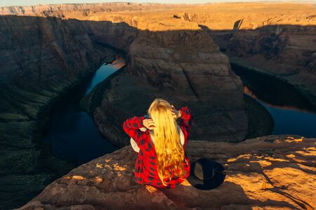 blonde girl sitting Horseshoe Bend in Glen Canyon National Recreation Area in early dawn.の写真素材