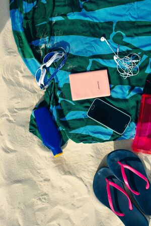 vacation and summer holidays concept - flip flops, towel, cap, bottled water and bottle of sunscreen oil on beach sand.の写真素材
