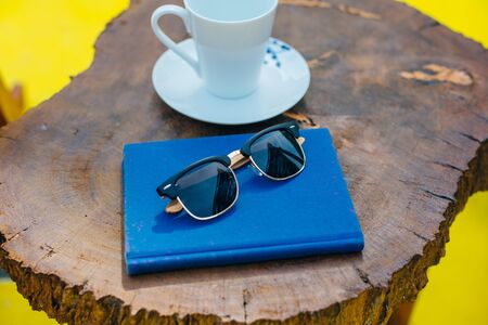wood sunglasses on a table with a blue book and a cup of coffee