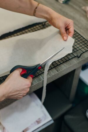 Hand holding up a sheet of baking paper and cut using a pair of scissors.の写真素材