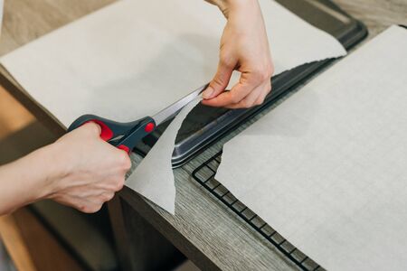 Hand holding up a sheet of baking paper and cut using a pair of scissorsの写真素材