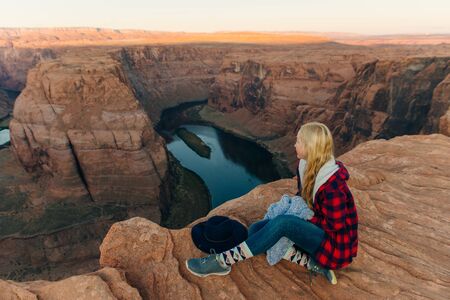 blonde girl sitting Horseshoe Bend in Glen Canyon National Recreation Area in early dawn.