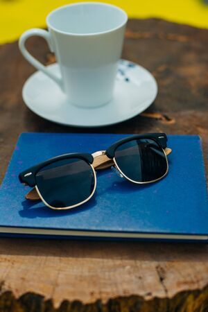 wood sunglasses on a table with a blue book and a cup of coffeeの写真素材