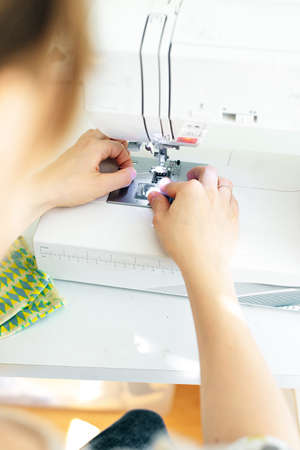 Female hands stitching white fabric on professional manufacturing machine at workplace. Seamstress...