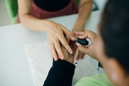 Manicurist applying cuticle softener or clear nail varnish to the fingernails of a lady client in a spa or beauty salon, close up of their hands.の写真素材