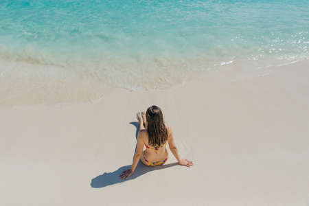 brunette girl in a bright swimsuit sitting on the beach in cancun, mexicoの写真素材