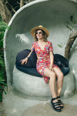 girl in a straw hat and a colored cape sits on a puffの写真素材