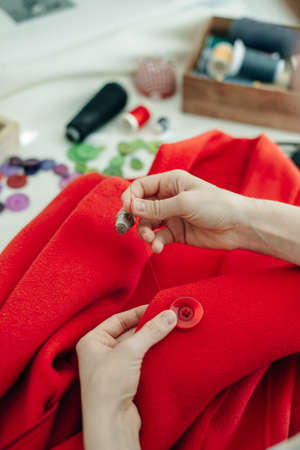 a seamstress sews a button on a red coat.の写真素材