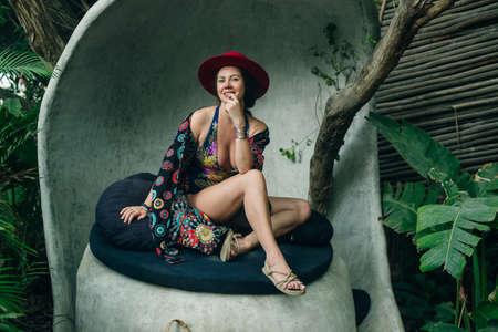 girl in a red hat and a colored cape sits on a puffの写真素材