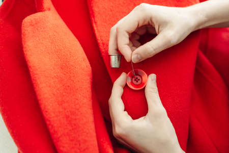 a seamstress sews a button on a red coat.の写真素材