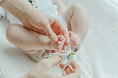 Mather hand holding scissors trimming child toenail