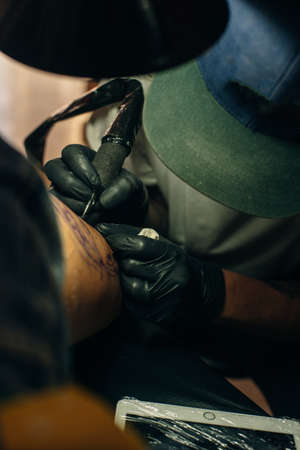 Close up of professional tattooer artist doing picture on hand of man by machine black ink from a jar. Tattoo art on bodyのeditorial素材