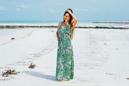 beautiful girl in sunglasses in a bright dress on a white beach.