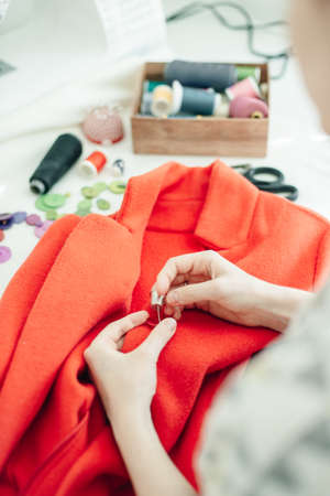 a seamstress sews a button on a red coat.の写真素材