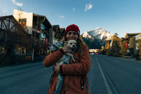 girl in an orange jacket holds a chihuahua in her arms near lake, canada.