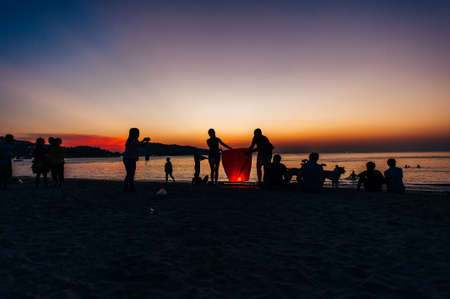 Silhouettes of people on the beach. Launching rice paper hot air balloons in the sky at sunset on a...