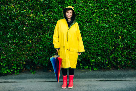 girl stands with his back in a yellow raincoat with an umbrella on a background of green wall.の写真素材