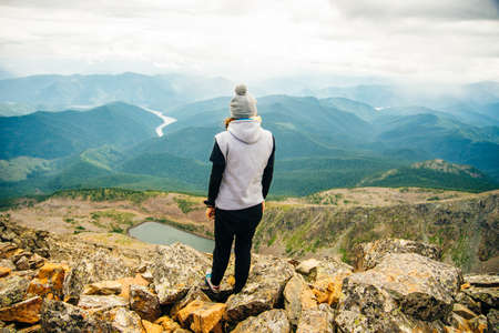 a girl in warm clothes stands with her back on the top with beautiful mountains and lakes. High quality photoの写真素材