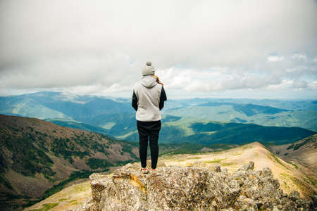 a girl in warm clothes stands with her back on the top with beautiful mountains and lakes. High quality photoの写真素材