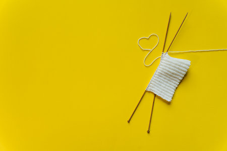 white wool knitting needles and a piece of knitting against a yellow background. high quality photoの写真素材