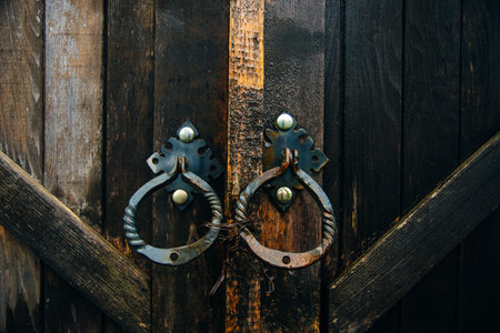 Close up of a heavy wooden plant double door, with iron hinges and handles, closing off the entrance into an old brick building. High quality photoの写真素材