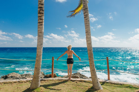 girl stands with her back against the blue ocean between palm trees. Cancun Mexico.の写真素材