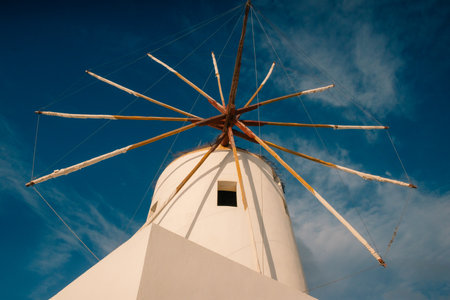 An old white mill stands on a top of the village of Oia, clear blue sky, dry grass in wooden boxes...