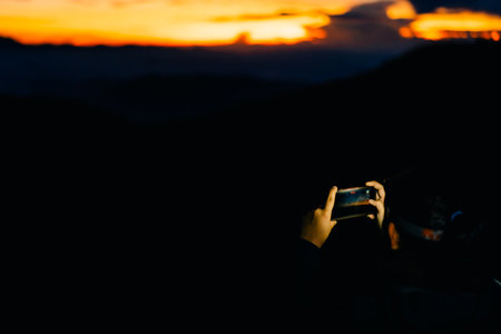 Girl filming sunrise in the mountains on her phone. High quality photoの写真素材