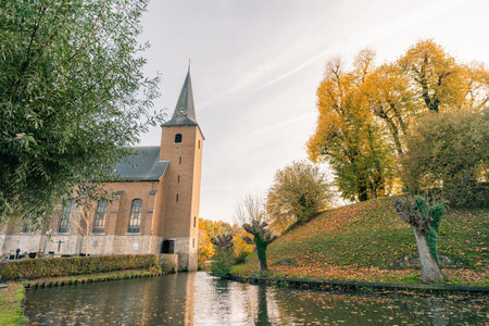 Wijnandsrade Castle moat between church and hill, reflection on surface, sunny autumn day in South Limburg, Netherlands - 1 Oct 2025. High quality photoの写真素材